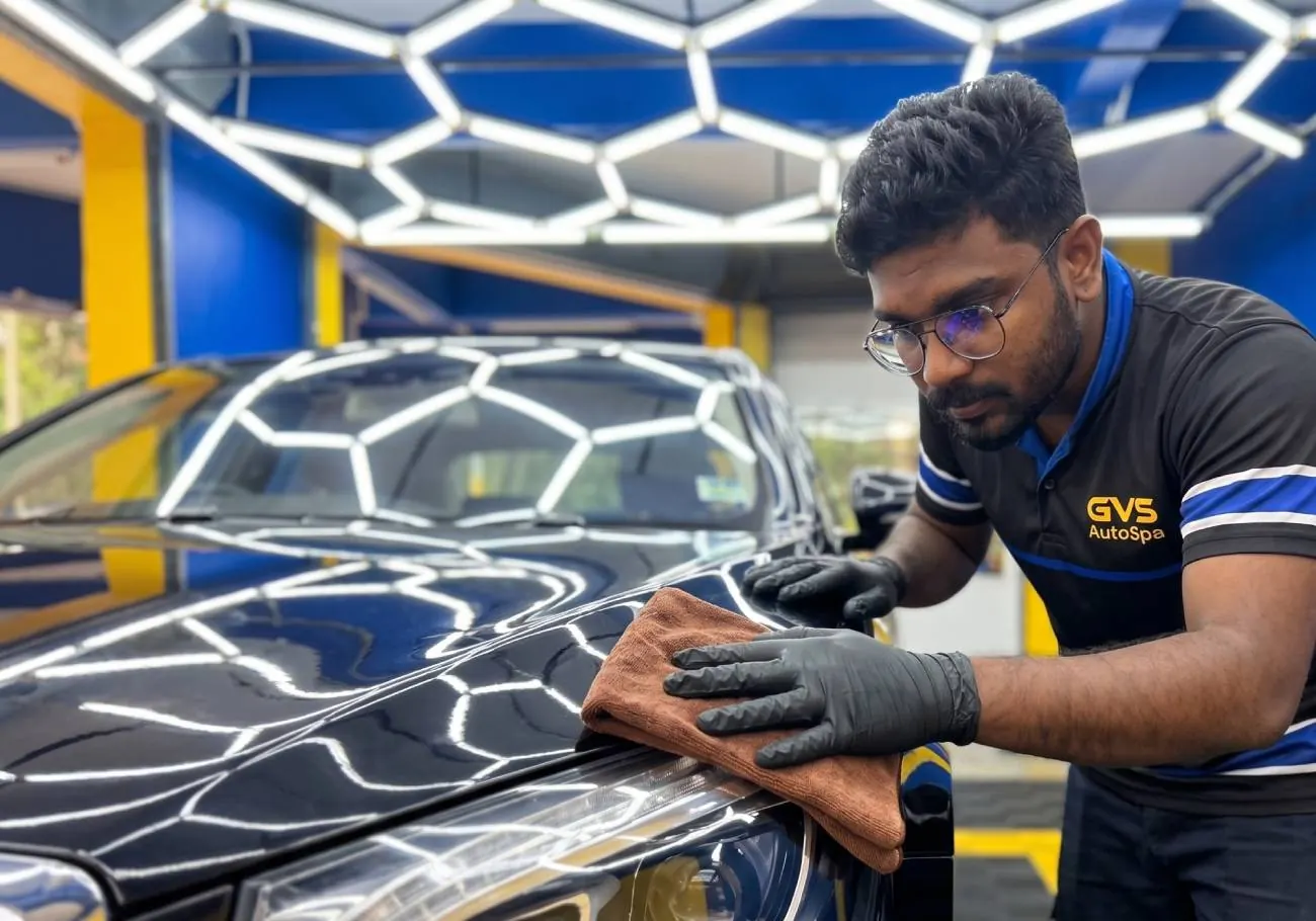 A GVS technician hand-finishing a black car under the hexagonal light rig